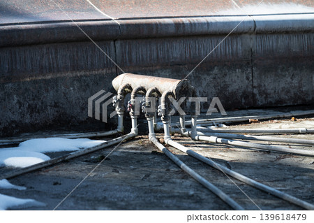 A metal pipe manifold with several curved pipes and valves connected to a central header. Water supply system pipes for a fountain in winter. A metal pipe manifold with several curved pipes and valves connected to a central header. Water supply system pipes for a fountain in winter. 139618479