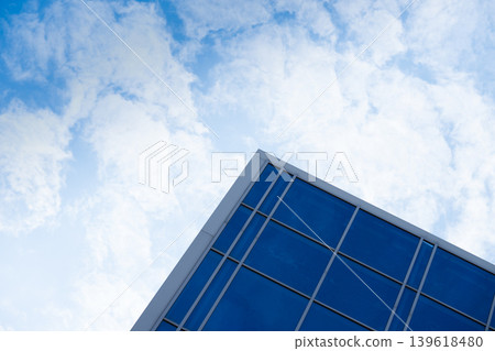 A minimalist architectural shot showing the corner of a modern office building with blue glass windows and a grey metal frame. A minimalist architectural shot showing the corner of a modern office building with blue glass windows and a grey metal frame. 139618480