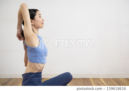 A middle-aged Japanese woman makes a cow face pose on a mat. 139618616