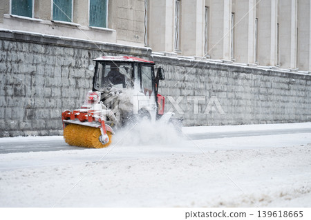 Compact municipal snow sweeper with rotary brush . A sweeper moves along a snow-covered street . Compact municipal snow sweeper with rotary brush . A sweeper moves along a snow-covered street . 139618665