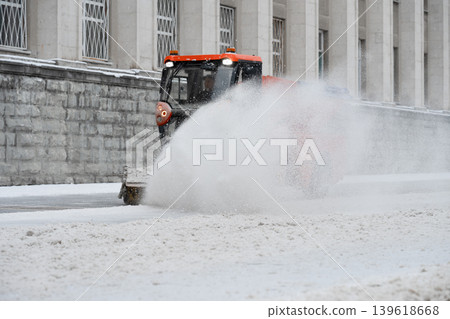 Compact municipal snow sweeper with rotary brush . Sweeper moves along a snow-covered street . Compact municipal snow sweeper with rotary brush . Sweeper moves along a snow-covered street . 139618668