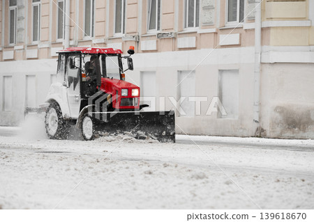 Red bright Tractor removing snow from sidewalk with steel blade . Red bright Tractor removing snow from sidewalk with steel blade . 139618670