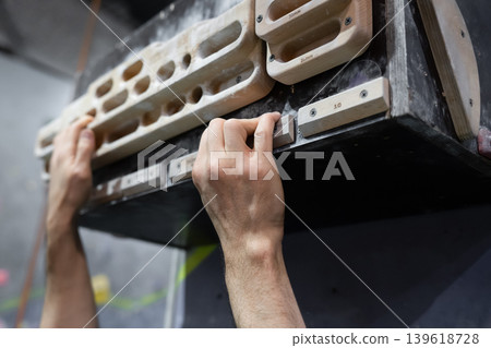 Close-up shot of hands gripping a climbing board with artificial holds. Indoor rock climbing and bouldering training concept focused on grip strength, technique, and physical effort. Close-up shot of hands gripping a climbing board with artificial holds. Indoor rock climbing and bouldering training concept focused on grip strength, technique, and physical effort. 139618728