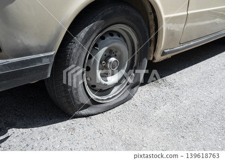 Close-up of a deflated tire on a classic beige car. The shot shows the flat rubber touching the grey asphalt road, emphasizing a breakdown, car trouble, or neglect. Close-up of a deflated tire on a classic beige car. The shot shows the flat rubber touching the grey asphalt road, emphasizing a breakdown, car trouble, or neglect. 139618763