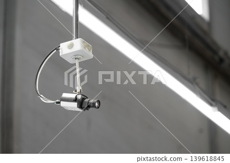 A ceiling-mounted surveillance camera installed on a metal conduit inside an industrial or commercial interior. Copy space 139618845