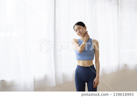 一位身穿瑜珈服的中年日本女性，一手搭在肩膀上，臉上露出痛苦的表情。 139618993