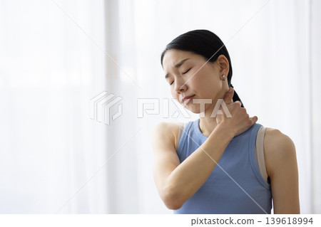 一位身穿瑜珈服的中年日本女性，一手搭在肩膀上，臉上露出痛苦的表情。 139618994