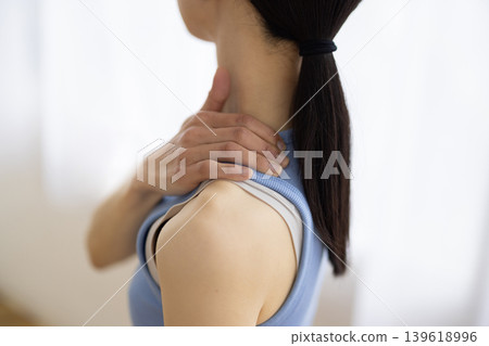 A middle-aged Japanese woman in yoga wear, with her hand on her shoulder and making a pained expression. A middle-aged Japanese woman in yoga wear, with her hand on her shoulder and making a pained expression. 139618996
