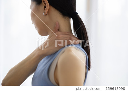 一位身穿瑜珈服的中年日本女性，一手搭在肩膀上，臉上露出痛苦的表情。 139618998