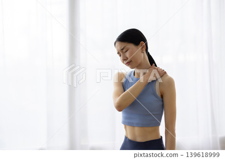 一位身穿瑜珈服的中年日本女性，一手搭在肩膀上，臉上露出痛苦的表情。 139618999
