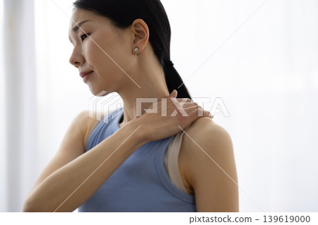 一位身穿瑜珈服的中年日本女性，一手搭在肩膀上，臉上露出痛苦的表情。 139619000