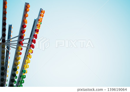 Abstract amusement park ride structure with colorful LED lights against a clear blue sky. Vibrant carnival ride details with red, yellow, and green lights and copy space for text. 139619064