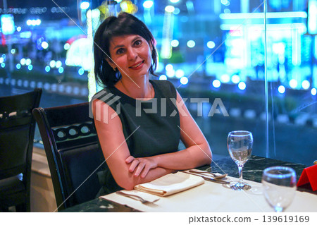 Elegant Woman Enjoying Dinner in a Restaurant with Stunning Night City View Through the Window, Capturing the Essence of Urban Sophistication 139619169