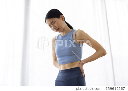 一位身穿瑜珈服的中年日本女性，雙手叉腰，表情痛苦。 139619267