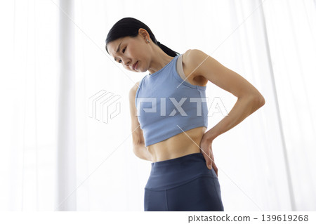 一位身穿瑜珈服的中年日本女性，雙手叉腰，表情痛苦。 139619268