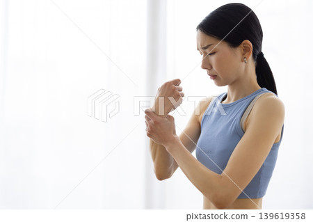 一位身穿瑜珈服的中年日本女性摸了摸手腕，露出痛苦的表情。 139619358