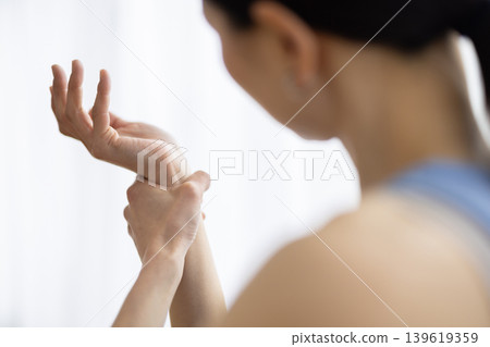一位身穿瑜珈服的中年日本女性摸了摸手腕，露出痛苦的表情。 139619359