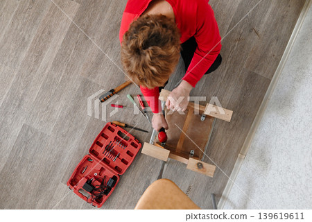 Woman repairing wooden furniture in a room with tools and materials on the floor Woman repairing wooden furniture in a room with tools and materials on the floor 139619611