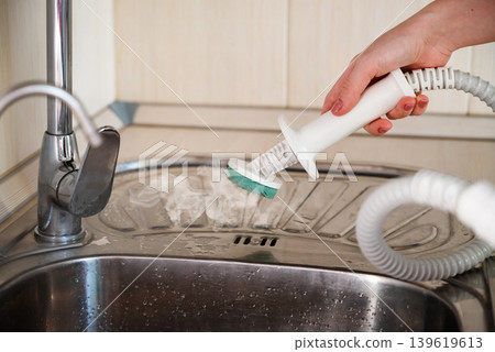 Cleaning the kitchen surface with a steam cleaner next to the sink at home Cleaning the kitchen surface with a steam cleaner next to the sink at home 139619613