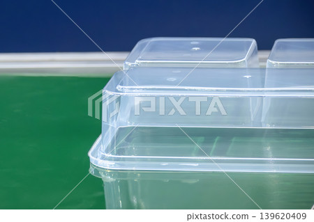 Close-up of clear plastic food container box parts moving on a conveyor belt in a high-standard manufacturing plant. Close-up of clear plastic food container box parts moving on a conveyor belt in a high-standard manufacturing plant. 139620409