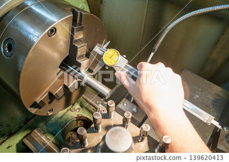 High angle shot of a skilled machine operator measuring a metal shaft part with a precision dial vernier caliper. High angle shot of a skilled machine operator measuring a metal shaft part with a precision dial vernier caliper. 139620413