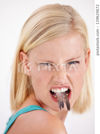 Woman, eating and portrait with fish, tail or dislike strange food in mouth on white background of studio. Crazy, diet and person with weird seafood, cuisine and disgust for taste of tuna or salmon 139620672