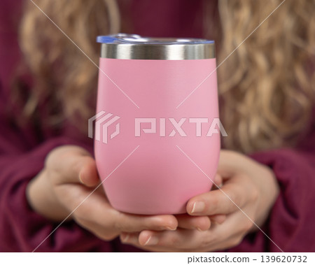 Blank pink 12 oz wine tumbler mockup in hands of young woman in red sweatshirt, copy space 139620732