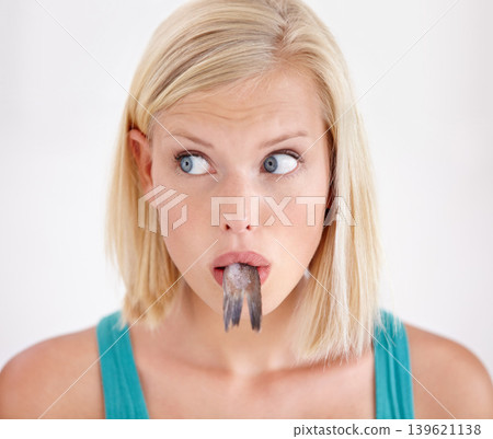 Face, woman and eating tail of fish with surprise and shock on white background of studio. Crazy, diet and person with taste of weird seafood, cuisine and confused with gross or strange food in mouth Face, woman and eating tail of fish with surprise and shock on white background of studio. Crazy, diet and person with taste of weird seafood, cuisine and confused with gross or strange food in mouth 139621138