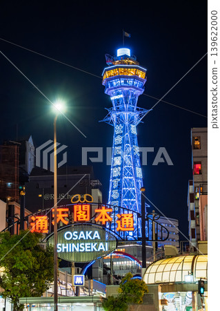 The blue-glowing night view of Tsutenkaku Tower seen through the neon arch of the Tsutenkaku Hondori shopping street in Osaka City. The blue-glowing night view of Tsutenkaku Tower seen through the neon arch of the Tsutenkaku Hondori shopping street in Osaka City. 139622000