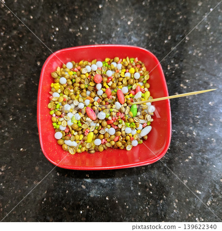 Top-down view of a vibrant mouth freshener mix in a square red bowl, placed on a dark, speckled kitchen countertop. 139622340