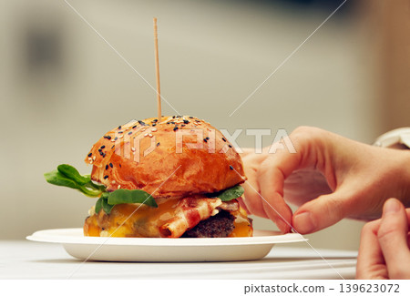 Juicy bacon cheeseburger with hand reaching for crumb Juicy bacon cheeseburger with hand reaching for crumb 139623072