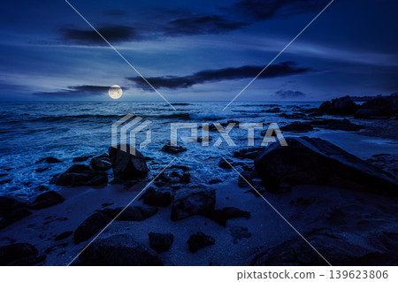 huge stones on a sandy beach at night. wonderful summer vacation season at the black sea. full moon over calm waves washing the sand shore. mysterious nature background with cloudy sky huge stones on a sandy beach at night. wonderful summer vacation season at the black sea. full moon over calm waves washing the sand shore. mysterious nature background with cloudy sky 139623806