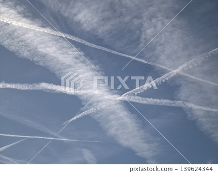 Contrails And Clouds In Open Blue Sky. Crisscrossed Vapor Streaks Under Expansive Daytime Sky Atmosphere 139624344