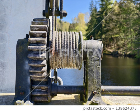 Antique Mechanical Device With Nature. Old Winch Mechanism Surrounded By Moss And Tranquil Water Antique Mechanical Device With Nature. Old Winch Mechanism Surrounded By Moss And Tranquil Water 139624373