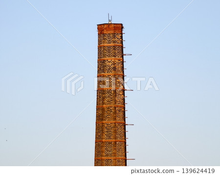 Old Tower Restoring. Restoring Ancient Brick Chimney With Scaffolding Amidst City Skyline Background Old Tower Restoring. Restoring Ancient Brick Chimney With Scaffolding Amidst City Skyline Background 139624419