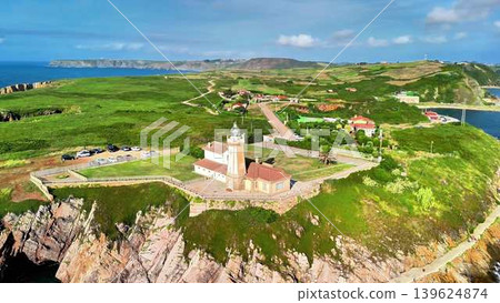 A stunning aerial view of a picturesque coastal lighthouse located on a vibrant green cliff A stunning aerial view of a picturesque coastal lighthouse located on a vibrant green cliff 139624874