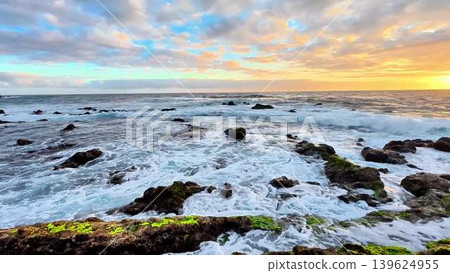 A stunning coastal sunset casts colorful reflections on dynamic waves and rocky shoreline 139624955