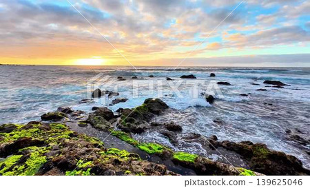 Experience the stunning beauty of a coastal sunrise over rocky shores and crashing waves 139625046