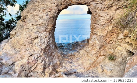 A beautiful, scenic rock arch perfectly overlooking a serene view of the ocean beyond 139625225