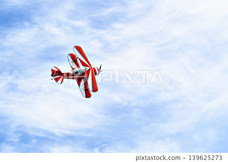 A red aerobatic biplane performing air shows in a blue sky with white clouds. Classic airplanes 139625273