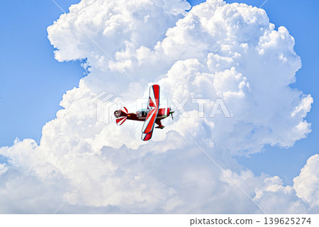 A red aerobatic biplane performing air shows in a blue sky with white clouds. Classic airplanes 139625274