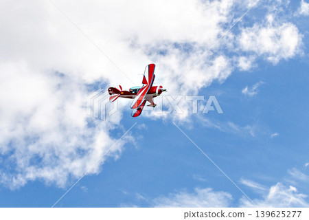 A red aerobatic biplane performing air shows in a blue sky with white clouds. Classic airplanes 139625277