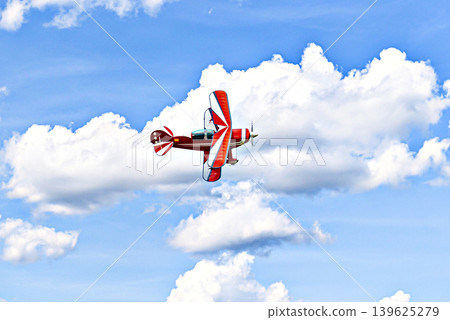 A red aerobatic biplane performing air shows in a blue sky with white clouds. Classic airplanes A red aerobatic biplane performing air shows in a blue sky with white clouds. Classic airplanes 139625279