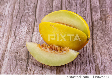Fresh ripe yellow melon with a slice and visible seeds on a rustic background. Fresh ripe yellow melon with a slice and visible seeds on a rustic background. 139625387