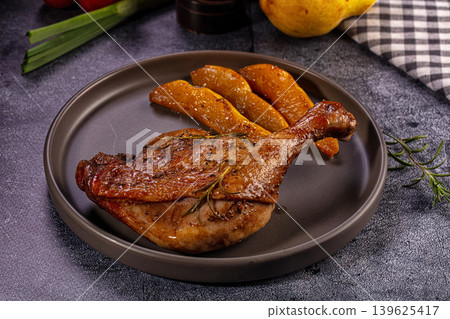 Gourmet roasted duck leg confit with caramelized pear slices and fresh rosemary on dark plate Gourmet roasted duck leg confit with caramelized pear slices and fresh rosemary on dark plate 139625417