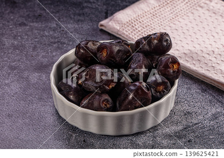 Medjool dates in white bowl. Dried sweet fruit on dark background with pink cloth Medjool dates in white bowl. Dried sweet fruit on dark background with pink cloth 139625421