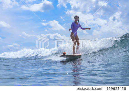 Energetic Woman Confidently Surfs Across Sunlit Blue Waters With Enthusiasm Energetic Woman Confidently Surfs Across Sunlit Blue Waters With Enthusiasm 139625456