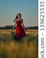 Woman rye field red dress. Happy woman in a long red dress in a beautiful cornfield. Old caste ruins in the background 139625535