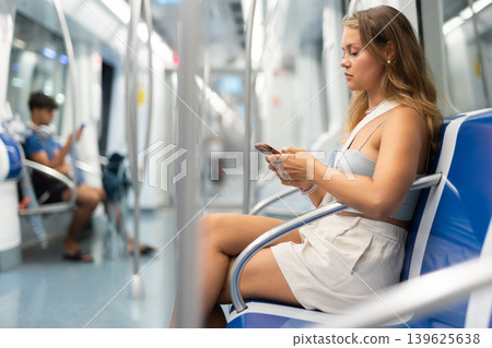 Young woman sitting in subway car with phone Young woman sitting in subway car with phone 139625638
