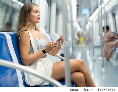 Young woman sitting in subway car with phone Young woman sitting in subway car with phone 139625641